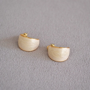 Detail of cream enamel earrings with gold plating and marble texture on fabric