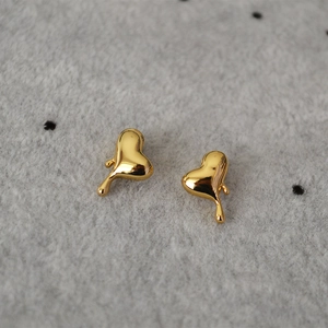 Detail der geschmolzenen Herz-Ohrstecker in Goldoptik auf grauem Stoffhintergrund