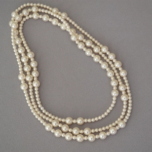 Close-up of elegant three-layer pearl necklace with varying bead sizes on grey fabric