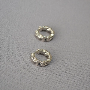Minimalist silver lava hoop earrings with irregular concave texture on gray fabric