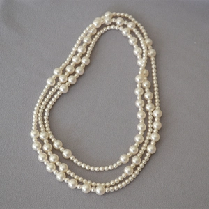 Three-layer layered pearl necklace with gradient white pearls on textured background