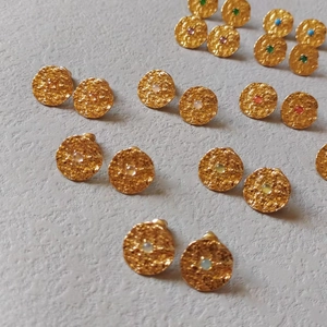 Macro view of textured gold earrings with colorful gemstones and hammered metal finish