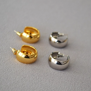 Detailed view of chunky C-shaped stud earrings in polished gold and silver finishes