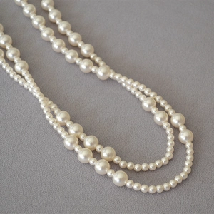 Detail of layered white pearl necklace with alternating sizes on linen background
