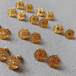 Macro shot of circular hammered gold earrings with multi-colored gemstone centers