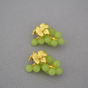 Macro shot of 925 silver stud earrings with golden vine leaves and green grape beads