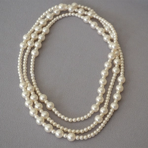 Close-up of triple-layered pearl necklace with round white pearls on a textured background