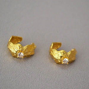 Detailed macro view of golden wavy textured earrings with sparkling round zircon center