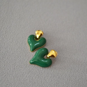 Detail of dark green enamel heart earrings with gold metal studs on grey texture