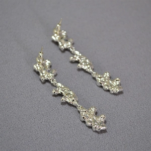 Detailed close-up of long liquid metal earrings with irregular lava texture in silver