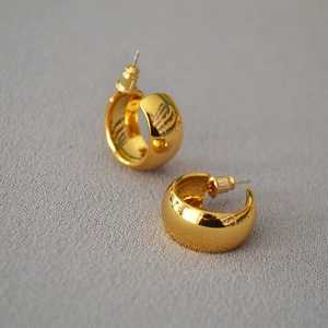 Detail of chunky gold C-shaped hoop earrings on textured grey fabric background