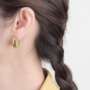 Close-up of modern gold-plated oval C-shaped hoop earrings worn by a model