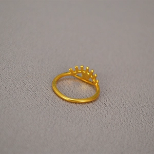 Detailed top view of a gold-plated brass eye-shaped open ring on a grey fabric texture