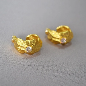 Macro shot of gold textured C-shape earrings with sparkling round zircon center