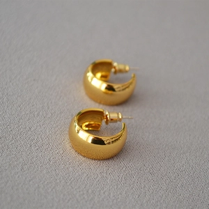 Close-up of chunky gold C-shaped hoop earrings with a high-shine polished mirror finish
