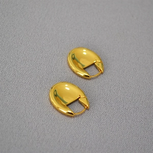 Close-up of thick oval hoop earrings with a polished gold finish on grey fabric