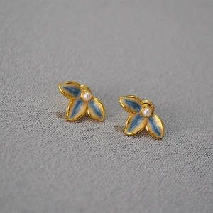 Floral enamel stud earrings with gold plating and central pearls on gray texture