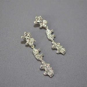 Close-up of long silver drop earrings featuring irregular molten lava texture and 925 posts