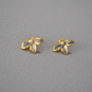 Detail of blue and white enamel flower stud earrings with a pearl center on gold base