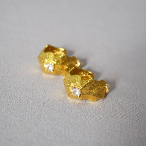 Detailed view of C-shaped gold-plated earrings with lava texture and central zircon stone