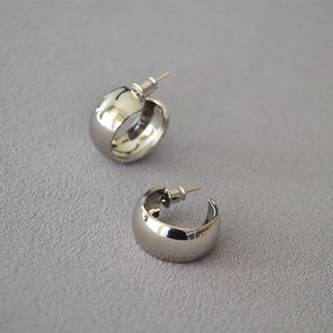 Minimalist wide silver C-shaped hoop earrings with polished mirror finish on grey fabric