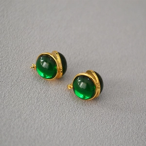 Vintage gold plated earrings featuring green glass beads on grey fabric background