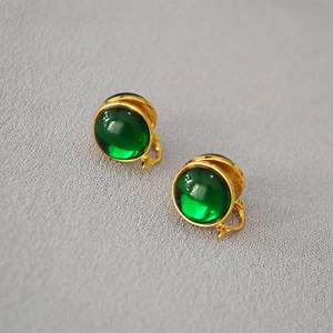 Macro detail of vintage gold-plated clip-on earrings with emerald green glass cabochons