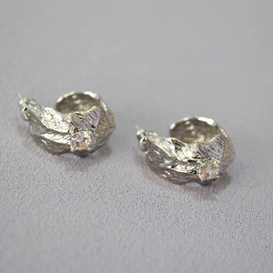 Macro detail of silver C-shaped earrings with unique tree bark texture and zircon stone