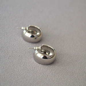 Macro detail of high-polished silver C-shaped chunky stud earrings on fabric