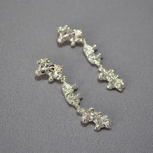 Macro view of long silver earrings with liquid metal lava texture and irregular surface