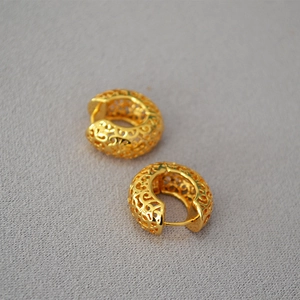 Macro shot of gold hoop earrings with intricate vintage hollow palace patterns and glossy finish