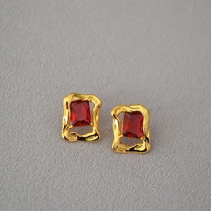 Close-up of gold irregular lava-textured earrings with rectangular red zircon stones