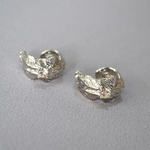 Detail of silver C-shape earrings with leaf texture and round cubic zirconia inlay