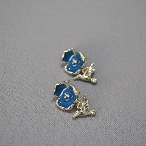 Macro view of blue enamel flower and silver bird earrings on textured fabric