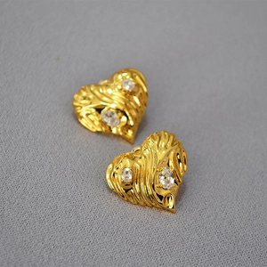 Detailed close-up of golden heart earrings with ripple texture and sparkling cubic zirconia
