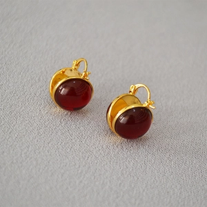 Detail of gold-plated hoop earrings with large round deep red cabochon stones and clasps