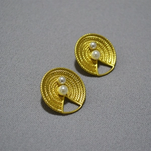 Détail de boucles d'oreilles en laiton doré vintage avec motifs et perles blanches
