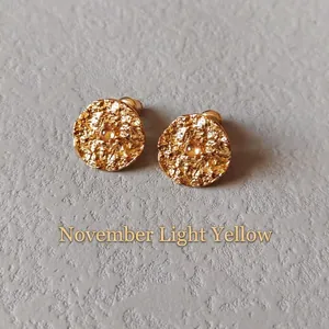 Detail of gold hammer-textured stud earrings with November pale yellow gemstones