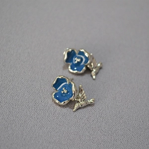 Detail of blue enamel flower stud earrings with delicate silver hummingbird charms