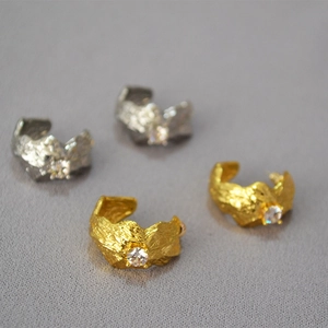 Detailed view of gold and silver textured earrings with a central sparkling zircon stone