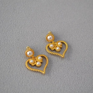 Detail shot of vintage heart-shaped gold earrings with white pearls on a textured background