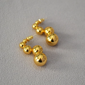 Close-up of gold beaded earrings featuring five polished spheres on a textured fabric