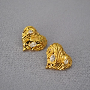 Macro detail of gold heart earrings with wavy texture and sparkling zircon stones
