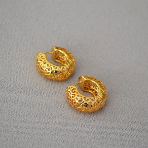 Detail of vintage gold hollowed-out ear hoops with intricate filigree pattern design