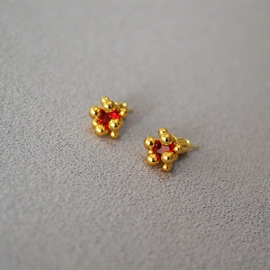 Macro shot of gold sphere stud earrings featuring a centered round red gemstone