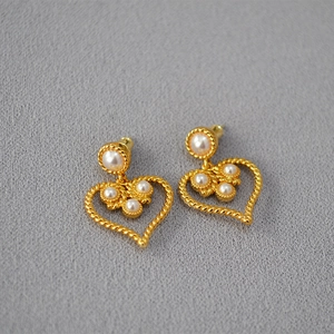 Detail of vintage gold heart earrings with faux pearls and intricate woven metal texture