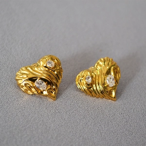 Macro detail of gold heart earrings with pleated texture and sparkling zircon stones