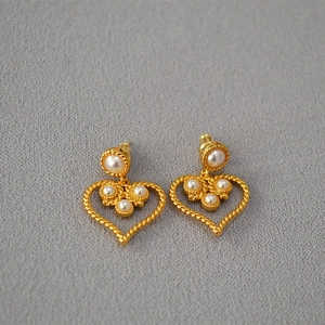 Detail of vintage gold heart earrings with white pearls on grey textured background