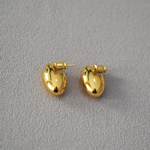 Detailed close-up of polished gold egg-shaped stud earrings on a textured grey background