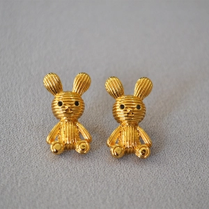 Close-up of golden 3D rabbit stud earrings with horizontal stripe texture and black dot eyes